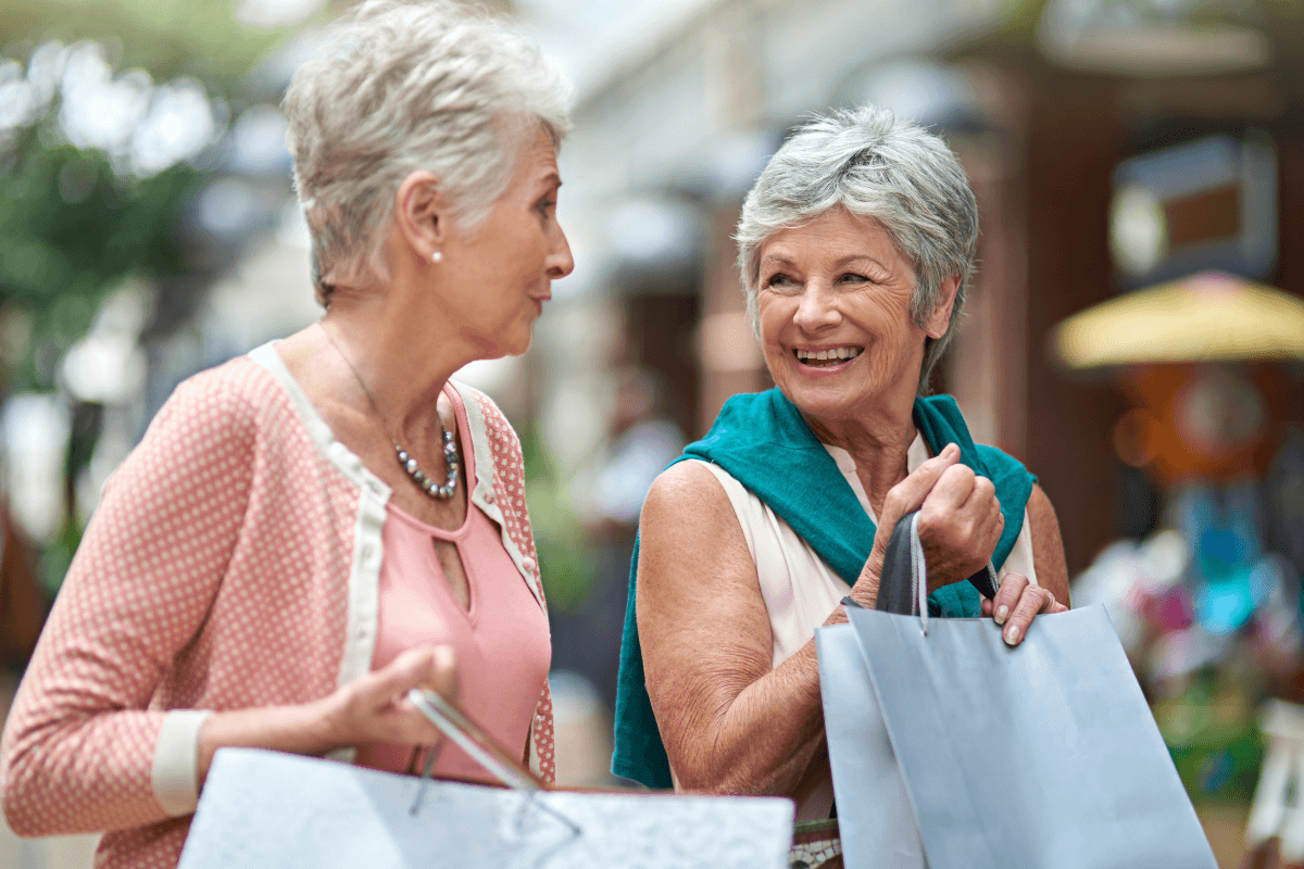 Two mature women shopping at a mall while holding shopping bags and smiling.